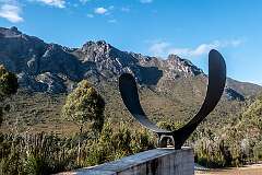 Bitumen Bones, a sculpture at the edge of the Gordon River Road; it is Alex Miles’s response to the “beautiful and often harsh environment” of south-west Tasmania. It has two parts: a quartzite rammed-earth wall to signify bleached bones; and black steel wings to represent the forest ravens that scavenge roadkill by the roadside.