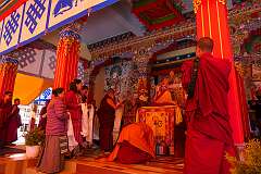 Prostrating before a throne with the cutout image of the founder of the monastery at the entrance to the monastery and women carrying “khata” ceremonial shawls.