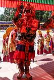 A masked dancer on the terrace of the monastery, with on the steps monks with ceremonial headdresses playing the Gya-Ling, a Buddhist ritual Reed Shawn.