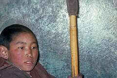 A young novice beating a large drum during the daily ritual in the monastery.