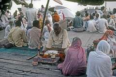 A fortune teller, seated under rattan umbrellas, reading fortunes for the visiting pilgrims on the banks of the Ganges river in Varanasi.